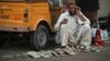 A labourer talks on his mobile phone as he sits beside his tools while waiting for work along a roadside